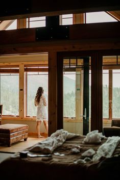 a woman standing in front of a bedroom window looking out at the mountains and trees