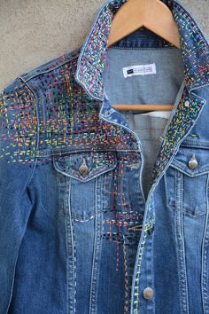 a denim jacket with multicolored patches on the front and back, hanging on a hanger