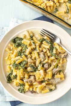 a white plate topped with pasta and spinach next to a casserole dish