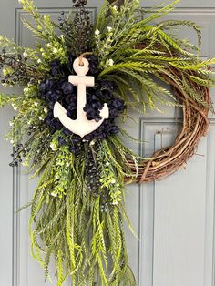 a wreath with an anchor is hanging on the front door, decorated with greenery