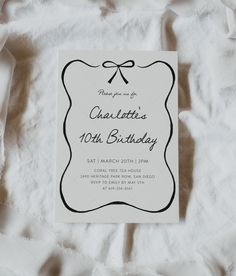 a white card with a black bow on it is laying on a bed and has the words charlotte's 10th birthday written in curs