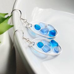 Gorgeous handmade sea glass earrings made with a mix of pale periwinkle, cobalt blue and clear beach glass. All captured in an oval shaped bezel with jewelers resin.  Simply lovely and eye catching! 🌿 *You will receive a UNIQUE pair of earrings with the same colors. Shape and size of sea glass pieces may vary. 🌿 Please see photo 3 for size reference. 🌿 Earring hooks are solid sterling silver. 🌿 Total earring length with hooks is 1.75 inches. Width is 15mm. 🌿 Oval Bezel is silver plated, and Blue Sea Glass Nickel Free Earrings, Blue Sea Glass Nickel-free Earrings, Nickel-free Blue Sea Glass Earrings, Handmade Blue Sea Glass Earrings, Nickel-free Blue Recycled Glass Earrings, Blue Recycled Glass Nickel-free Earrings, Blue Nickel-free Recycled Glass Earrings, Blue Teardrop Sea Glass Earrings, Blue Recycled Glass Dangle Earrings