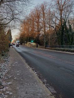 an empty street with snow on the ground and bare trees in the backgroud