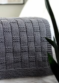 a gray knitted pillow sitting on top of a bed next to a potted plant