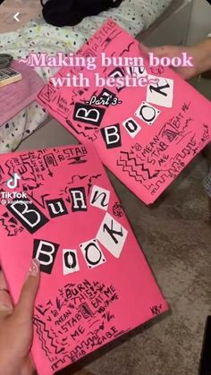 three pink books with writing on them are being held up by someone's hand