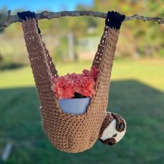 a crocheted slotty hanging from a tree with flowers in it's mouth