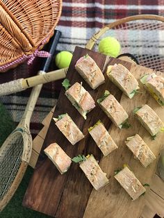 several sandwiches on a cutting board with tennis rackets and balls in the back ground