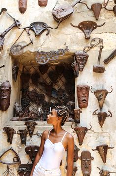 a woman standing in front of a wall with various masks on it's face