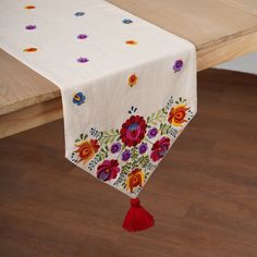 an embroidered table runner with flowers and tassels hanging from the edge on a wooden table