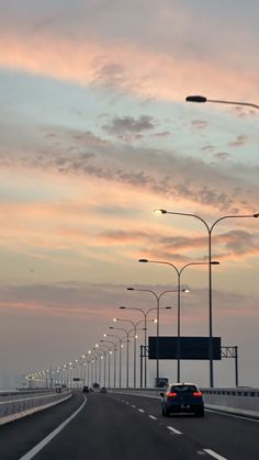 cars are driving down the highway at sunset or dawn with street lights on either side