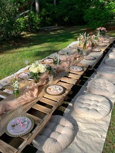 a long table set up with plates and napkins for an outdoor dinner in the grass