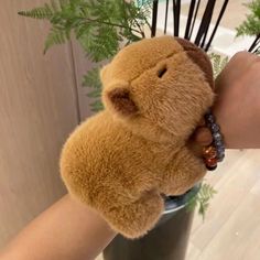 a person holding a teddy bear in a cup filled with plants and beads on their wrist