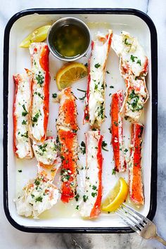 lobsters with lemon, parsley and garlic on a white plate next to a small bowl of dipping sauce