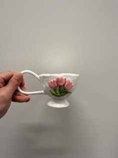 a hand holding a white cup with pink flowers on it