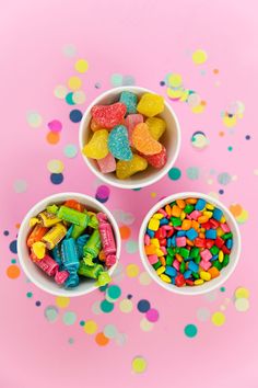 three bowls filled with candy on top of a pink table covered in confetti