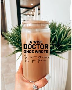 a person holding up a drink in front of a potted plant with the words a wise doctor once wrote on it