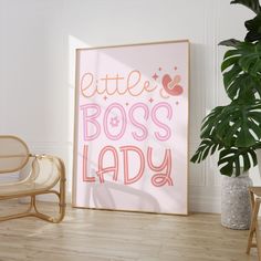 a pink poster with the words'little boss lady'on it next to a chair and potted plant