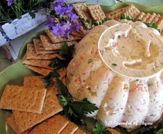 a platter filled with crackers and dip surrounded by purple flowers on the side