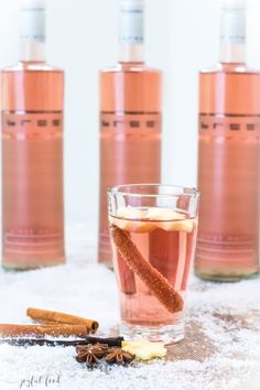 three bottles and two glasses filled with different types of liquid next to cinnamon stick, star anisette, and cloves