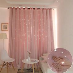 a living room with white furniture and pink curtains on the windowsill, while a person holds their hand up in front of them