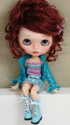 a doll with red hair sitting on top of a counter next to a wall and wearing blue boots