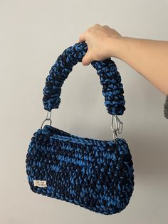 a hand holding a blue crocheted purse over a white wall with the handle down