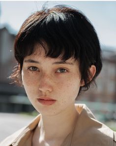 a woman with freckled hair is looking at the camera while wearing a tan shirt