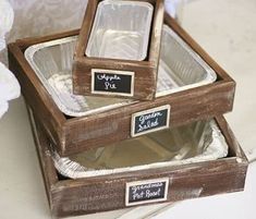 two wooden boxes with labels on them sitting on a table next to some white flowers