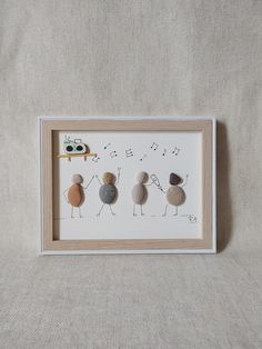 three pebbles are arranged in a frame on a white surface, one is holding a pencil and the other two are rocks