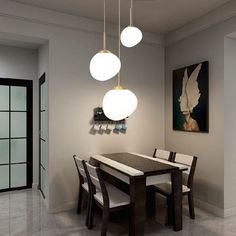 a dining room table with four lights hanging from it's ceiling and an art piece on the wall