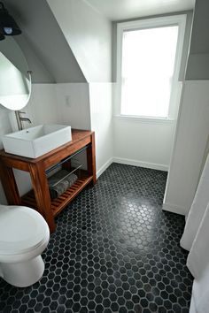 a white toilet sitting next to a sink in a bathroom under a window with a wooden cabinet