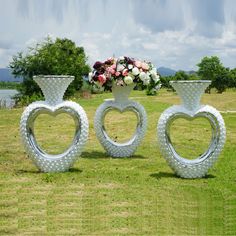 three white vases with hearts on them are in the middle of a field next to a flower arrangement