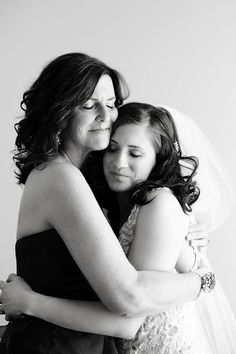 two women hugging each other in front of a white wall and one woman is wearing a veil