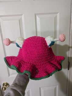 a hand is holding a pink crocheted hat