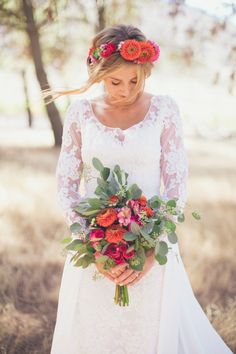 a woman in a white dress holding a bouquet and wearing a red flower headpiece