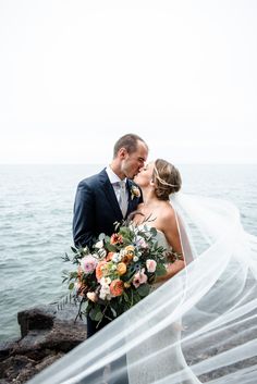 a bride and groom kissing by the ocean