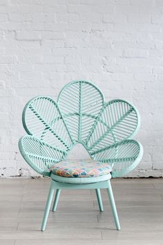 a green chair with a flower shaped seat cushion on it's back in front of a white brick wall