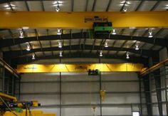 an overhead crane in a large warehouse with lights on it's sides and yellow beams