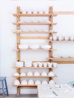 the shelves are filled with white dishes and bowls on wooden shelvings in front of a blue stool