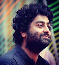 a man with curly hair and beard standing in front of a colorful wall wearing a black shirt