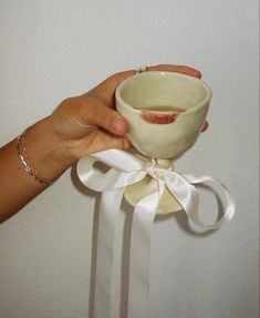 a hand holding a small cup with a white ribbon around it