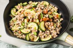 a skillet filled with zucchini, meat and other vegetables on top of a table