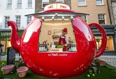 a large red teapot shaped like a restaurant with a man behind it in front of some buildings