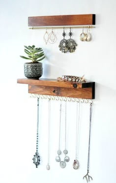 a wooden shelf with jewelry hanging from it's sides and a potted plant next to it