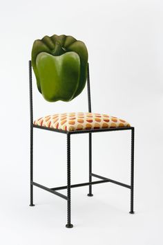 a green pepper sitting on top of a metal chair with a patterned seat pad underneath it