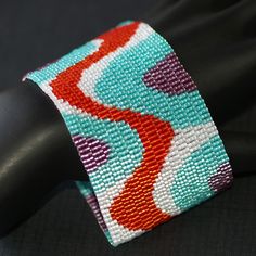 a close up of a colorful bracelet on a black cloth material with an orange and blue design