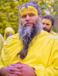 a man with a long beard and yellow face paint is standing in front of other men