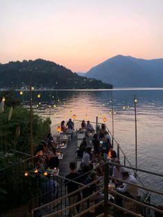 people are sitting at tables on the dock by the water with lit candles in front of them