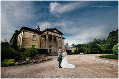 a bride and groom standing in front of a large building on a gravel road with trees around it