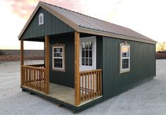 a small green house with a porch on the front and second floor, sitting in an empty lot